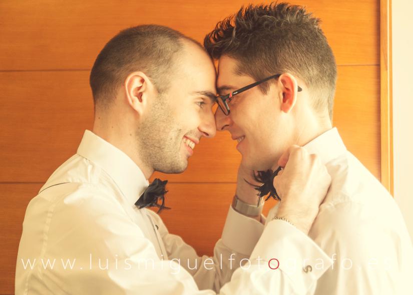 Pareja gay cruzan miradas de felicidad mientras se ayudan a vestirse para su boda